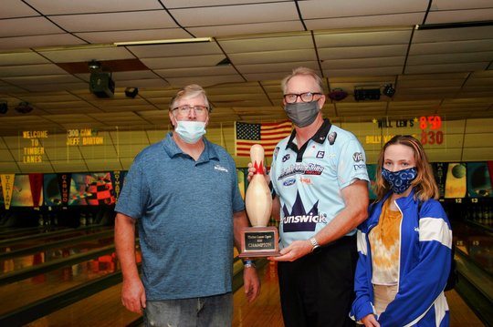 three men holding a trophy in front of the bowling lanes